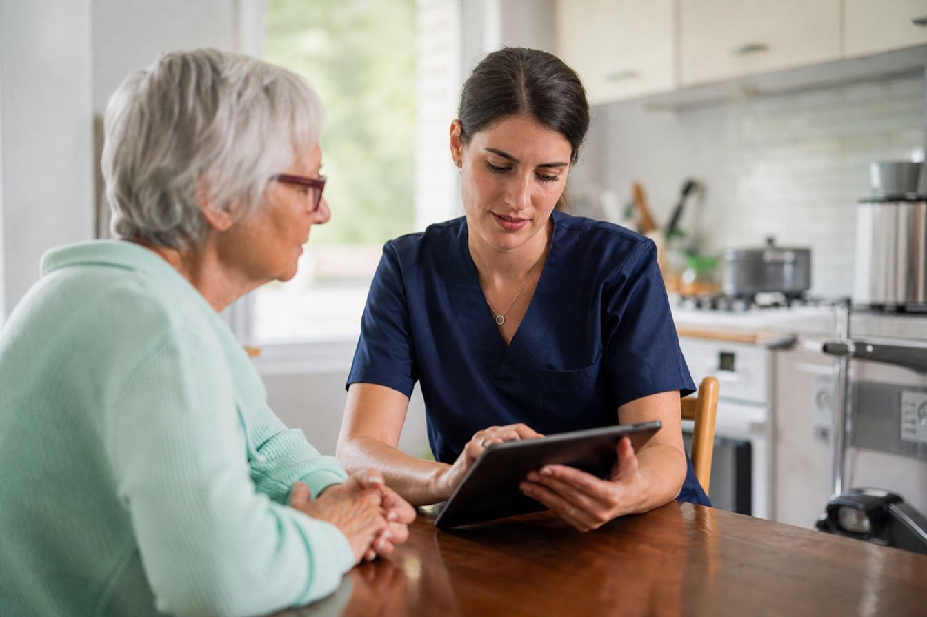 Infirmière libérale évaluant un plan de soins BSI sur tablette au domicile d'un patient